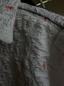 Cendre Cross White — close-up on the hanger, red hand-dyed crosses across the crinkled white ash-texture surface at shoulder and chest